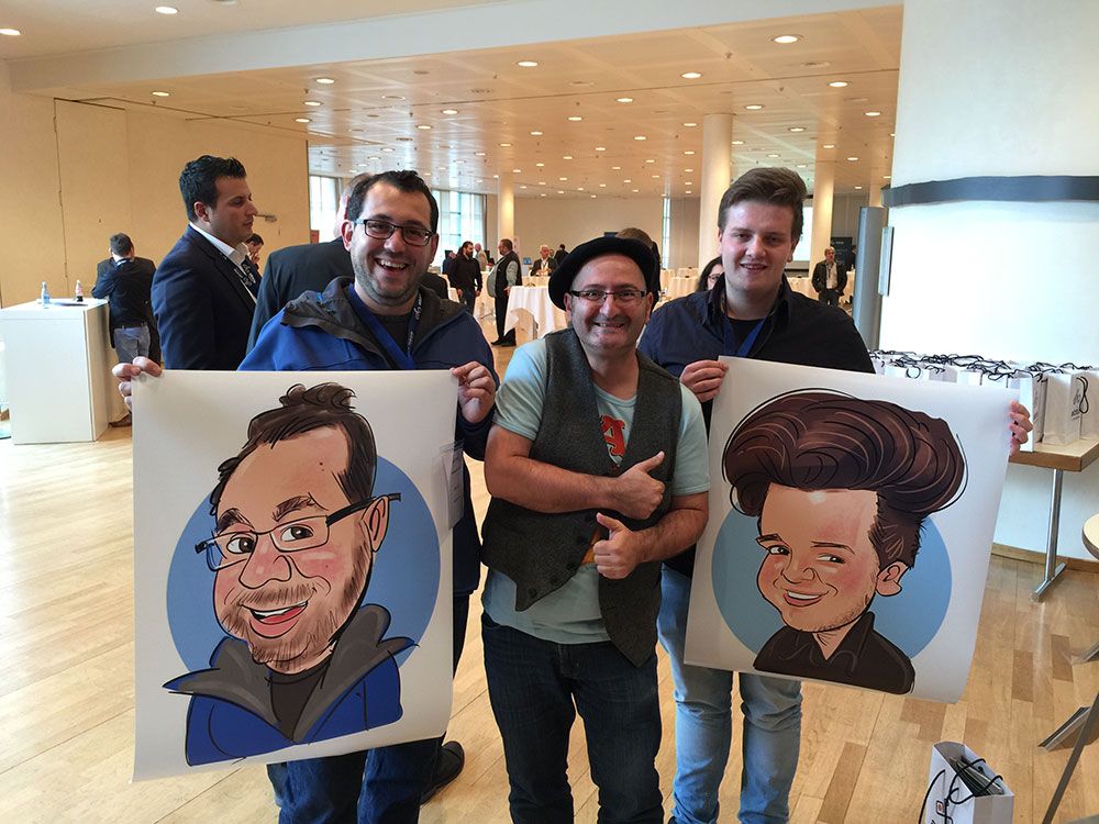 Erol steht zwischen zwei jungen Männern auf einer IT-Messe in Pforzheim; beide halten stolz XXL-Ausdrucke ihrer zuvor auf dem iPad gezeichneten Karikaturen, die im Rahmen einer Plotter-Vorführung erstellt wurden.