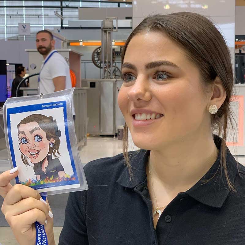 Eine junge Frau hält ihre fertige iPad-Karikatur auf der Paint Expo Messe in Karlsruhe neben sich und präsentiert stolz das Ergebnis.